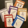 The fronts of the 7 colored cards for Haunted Inheritance: Red skeleton, blue pillowcase with $120,000, orange Sunrise, purple wound card with a picture of a band-aid, black Gathering Storm card, Gold Messenger Angel, and grey Zombie card