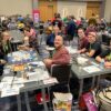 Two tables set up with the Haunted Inheritance game tournament. Nine players sit around the tables