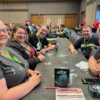 Five people sit around a table with the card game 'The Crew: Deep Sea Mission" on the table in front of them.