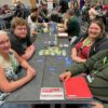 Four people sit around the table with the card game 'Float Your Boat' displayed and set out before them.